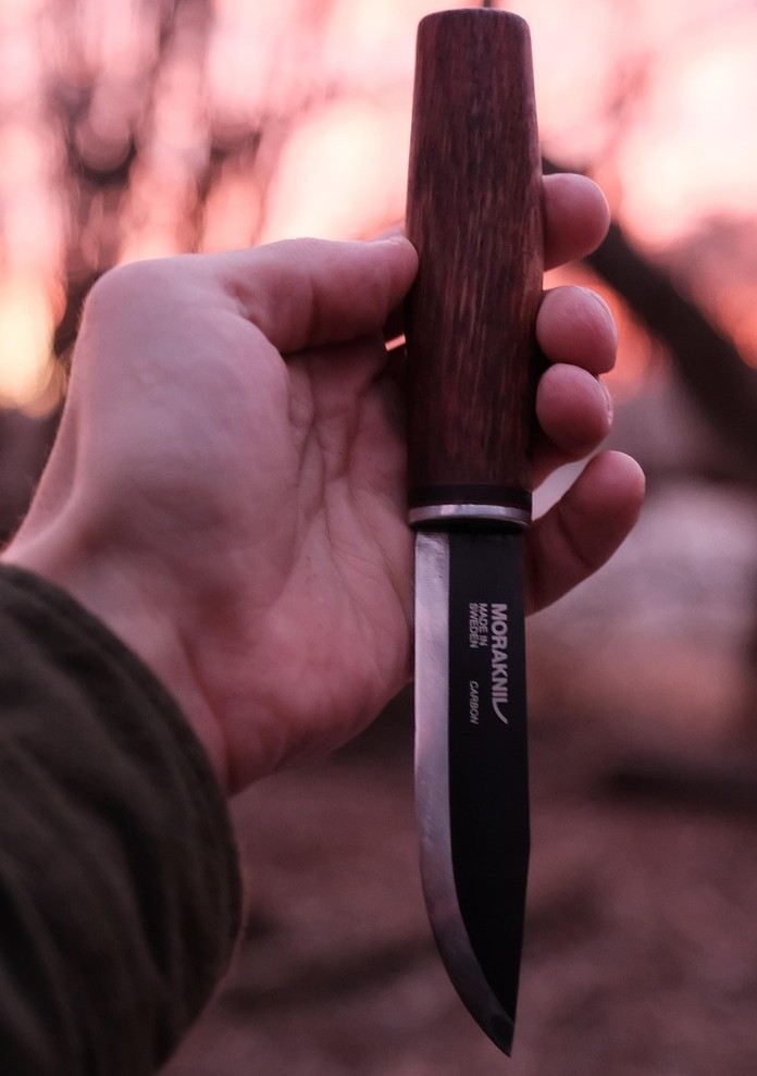 Hand holding a Morakniv style fixed blade knife at sunset – representative image